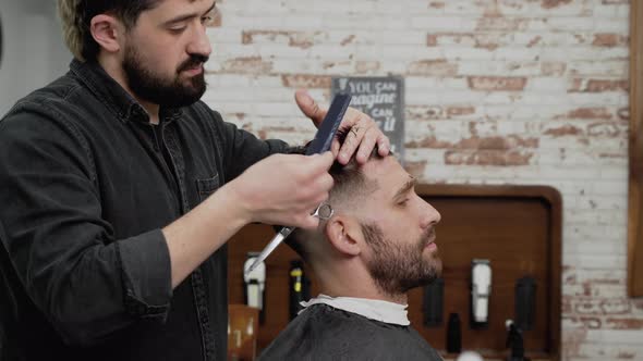 Barber Cutting Hair with Scissors to a Handsome Young Man