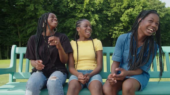 Cheerful Adorable African Teenage Sisters Resting and Talking on Park Bench