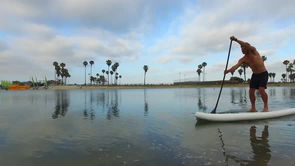 Tracking view of a man paddling his SUP stand-up paddleboard in a lake