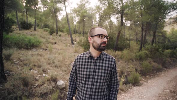 Young Caucasian Man In Sunglasses Admiring Trees And Scenery While Walking In Forest Track.