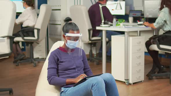 Black Businesswoman with Mask Against Covid19 Working on Armchair