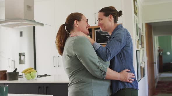 Caucasian lesbian couple smiling and dancing in kitchen