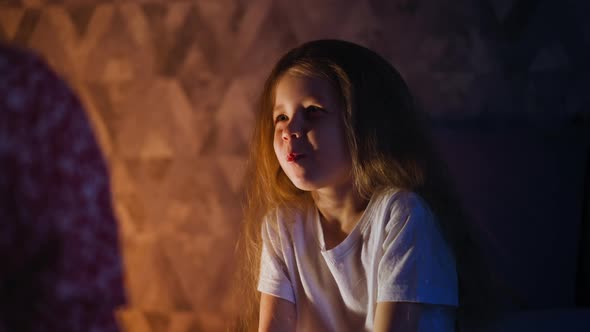 Pretty Little Girl Chews Food Looking at Parent in Dark Room