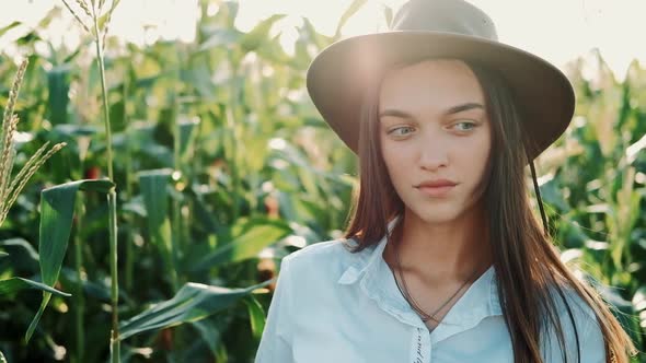 Portrait of Beautiful Young Girl in Hat Standing at a Corn Field Smiling and Looking at Camera in