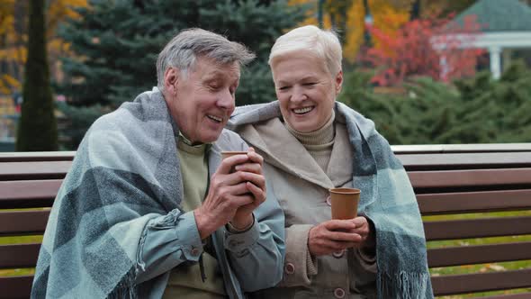 Joyful Pensioners Sitting in Park Drinking Hot Coffee Spouses in Warm Plaid Enjoy Conversation