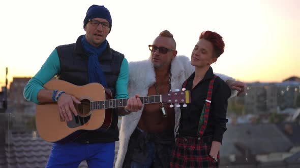 Confident Skilled Man Playing Guitar Singing for Friends Standing on Roof at Sunset