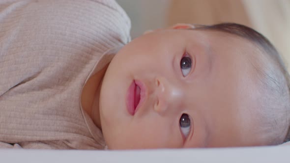 An Asian newborn baby is laying down on a soft white sheet mattress