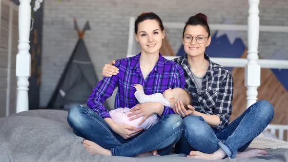 Two Smiling Female Parent Enjoying Motherhood Holding Sleeping Little Cute Baby By Hand