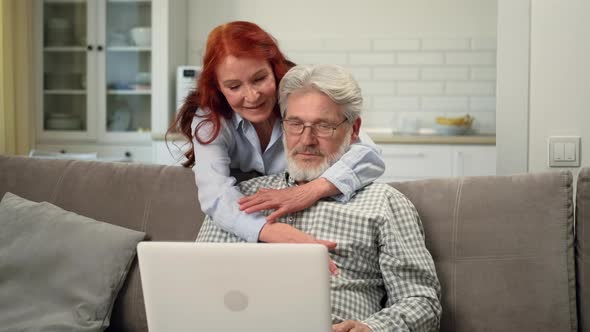 Senior Man is Sitting on the Couch Using a Laptop