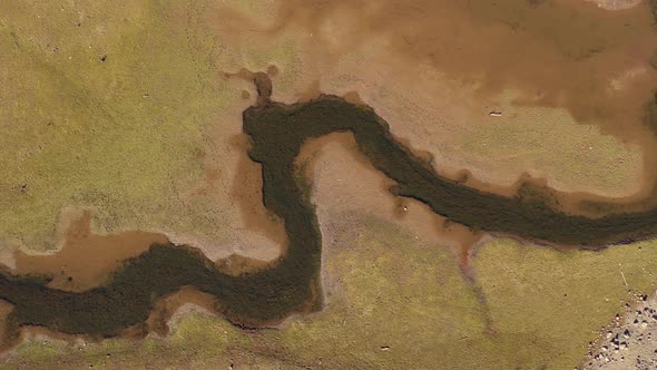 Aerial top down view of small river flowing through dry land on a hot summer day.