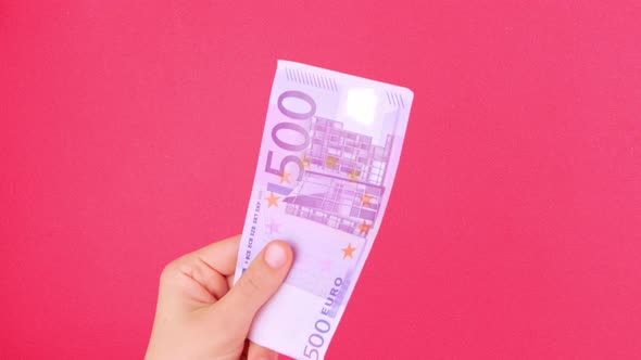 Hand in holds 500 EURO money bill on pink color background Counting cash european banknote exchange