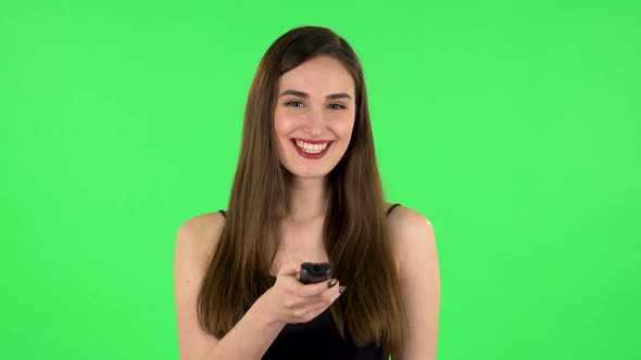Woman with TV Remote in Her Hand, Switching on TV and Very Laughs. Green Screen. Green Screen
