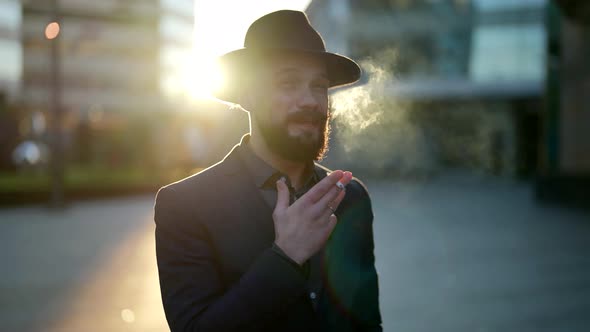 Smoking Man with Hat and Stylish Moustache is Standing Alone Outdoors in Sunny Evening