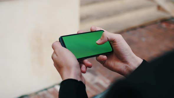 Man Using Smartphone in Horizontal Mode with Green Mock-up Screen Outside Urban City Business Office