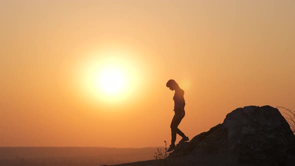 Silhouette of a Woman Hiker Climbing Alone Down From a Big Stone at Sunset in Mountains