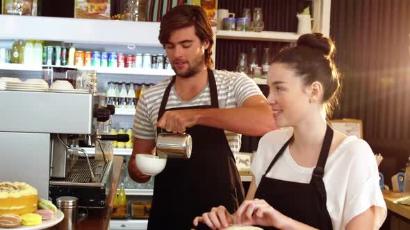 Waitress wrapping sandwich while waiter pouring milk in a cup