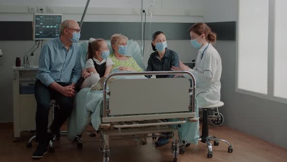 Medic Explaining Diagnosis to Aged Patient and Visitors in Hospital Ward