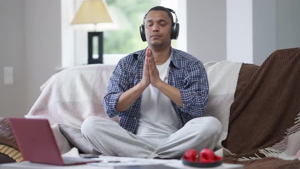 Wide Shot of Confident African American Man in Lotus Pose Sitting in Home Office Calming Down