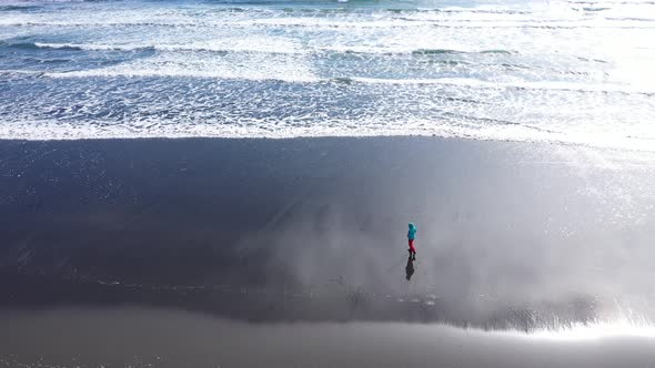 Aerial View of a Female Traveler Relaxing on Ocean Coast, Sea Waves Washing Beach, Iceland