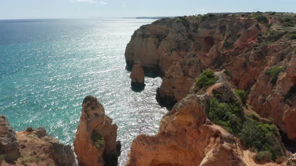 Flying over cliff towards a tall rock standing in the sea