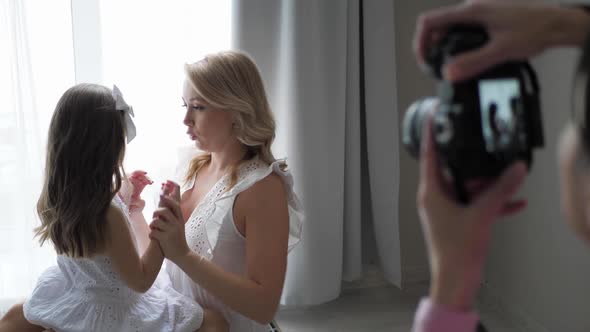 Beautiful Family Mother and Daughter in White Dresses are Sitting on the Floor By Large Window