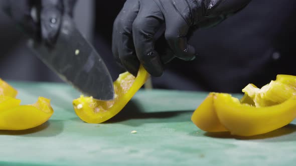 Cook's Hands in Black Gloves Chopping Yellow Peppers Close Up