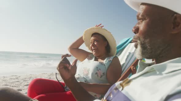 Smiling senior african american couple lying on sunbeds on sunny beach