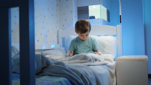 Little 5 Years Old Boy Using and Playing on Tablet Computer Before Going To Sleep at Night