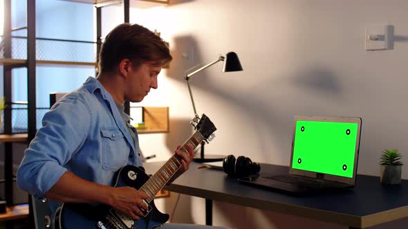 Young Man with Laptop Playing Guitar at Home