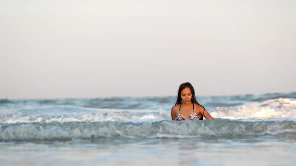 Girl with Wet Hair in a Leopard Swimsuit Splashes Water While Sitting in the Sea