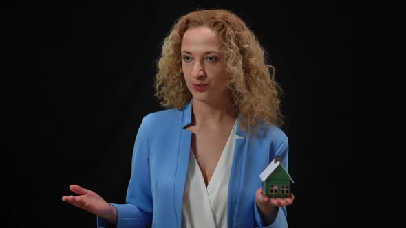 Inspired Serious Caucasian Woman Talking Holding Toy House in Hand