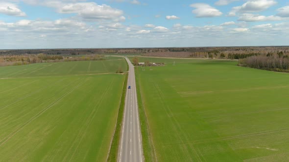 aerial drone view of rural road with cars moving on the right and left in the form of green fields i