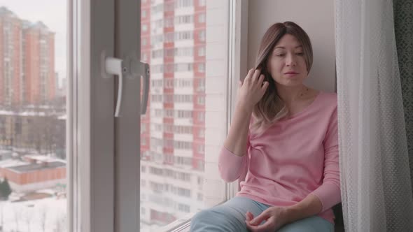 Woman with Curly Hair and Pink Longsleeve Is Sitting on Windowsill