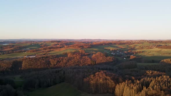 Aerial footage of small villages and colourful trees at sunset in west Germany. Pull back shot revea