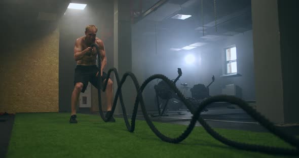 Male Athlete Working Out with Ropes in Old Building. Athlete Man in Training with Ropes Near Mirror