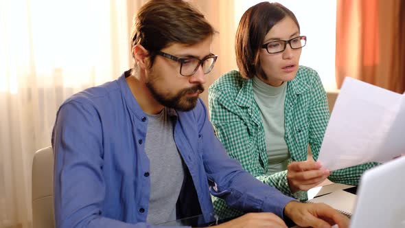 Serious Young Couple Holding Papers Pay Domestic Bills Online on Laptop