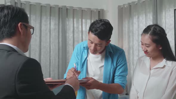 Asian Man With A Woman Signs On House Purchase Contract And Shaking Hands With A Real Estate Agent