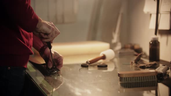 A Man Screws Bolts on a Leather Belt By the Table in a Workshop