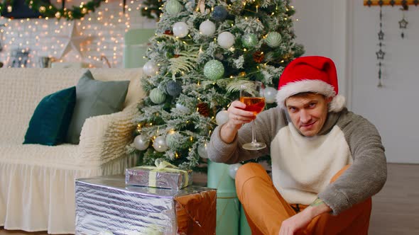 Young Man in Santa Hat Sitting on Floor Surrounded By Gift Boxes and Christmas Tree