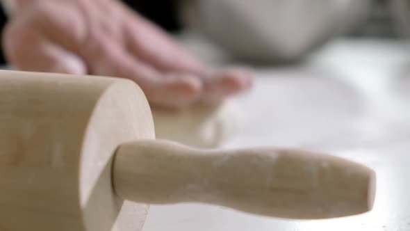 chef in kitchen bakery makes dough for pizza rolls out dough with rolling pin.