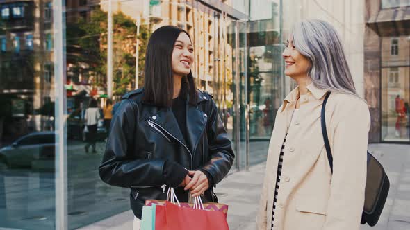 Asian Middleaged Mum and Adult Daughter Smiling Talking Holding Shopping Packages While Standing