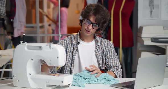 Young Man Tailor with Laptop Having Video Chat with Customer Discussing Fabric