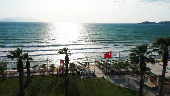 Turkish flag is waving in wind on sandy beach, famous tourist destination in Kusadasi. Palm trees, s