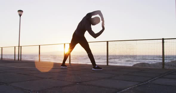 Focused african american man exercising outdoors, stretching by seaside at sunset