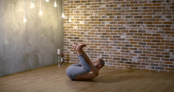 A Muscular, Lithe, Bearded Man Does Yoga in a Gym Against a Brick Wall, He Sits on a Transverse