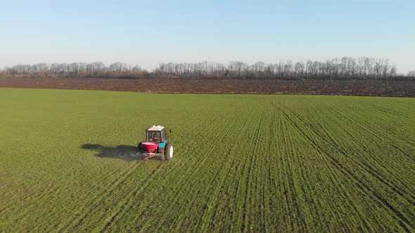 Aerial View of the Tractor Fertilizing the Chemicals on the Large Green Field.