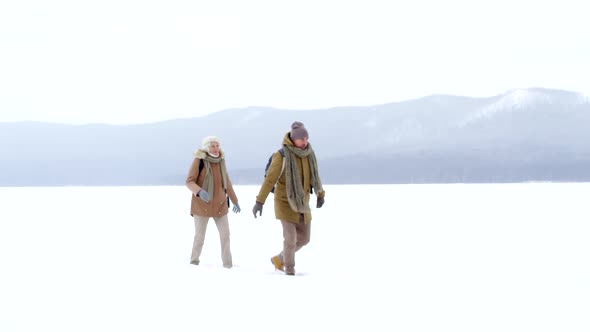 Retired Caucasian Couple Walking in Deep Snow over Frozen Lake