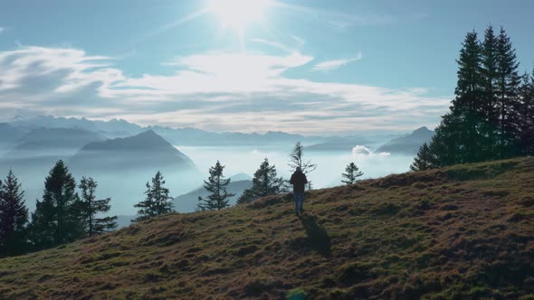 guy walking on a mountain ridge looking into beautiful mountain scenery with fog covered lake sunny