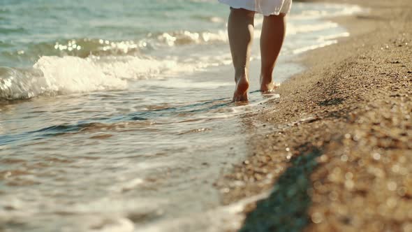 Slender Female Legs Walking Along the Sea Waves on a Sandy Beach