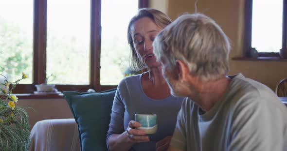 Smiling senior caucasian couple talking and drinking coffee in living room